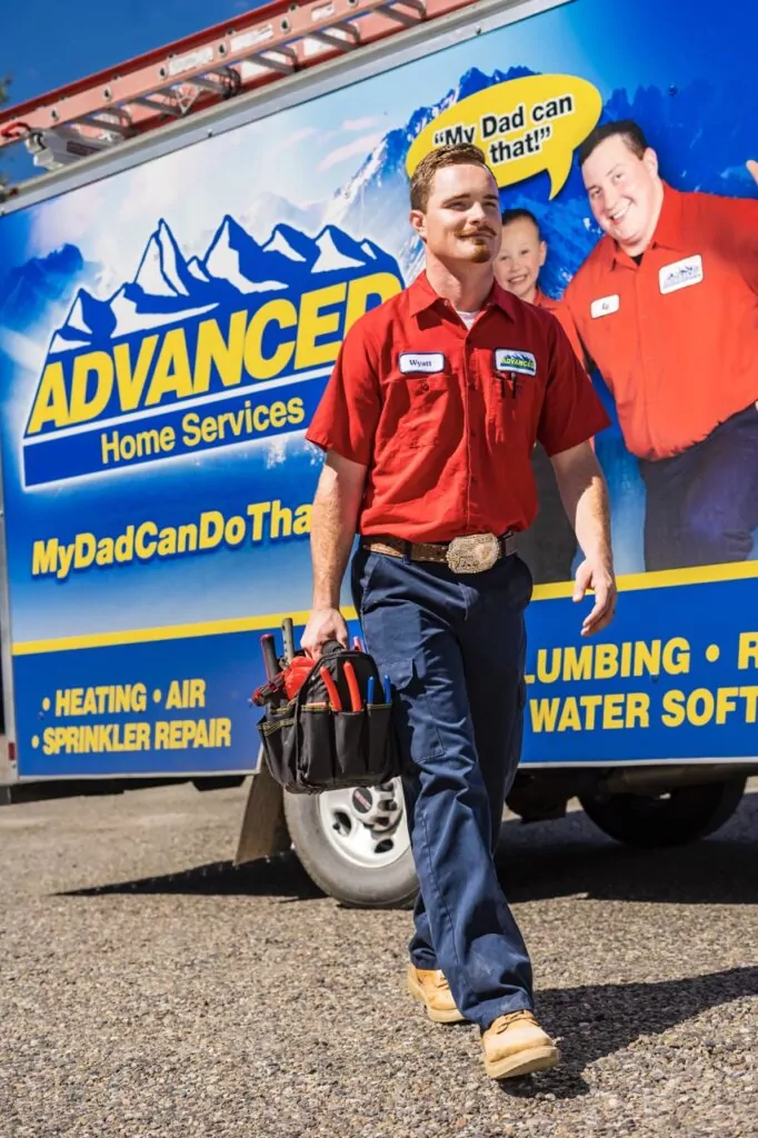 Advanced Home Service plumbing specialist arriving for service, carrying tool bag and walking past large service truck.