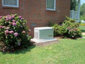 A whole home generator sits next to a house with bushes on either side.
